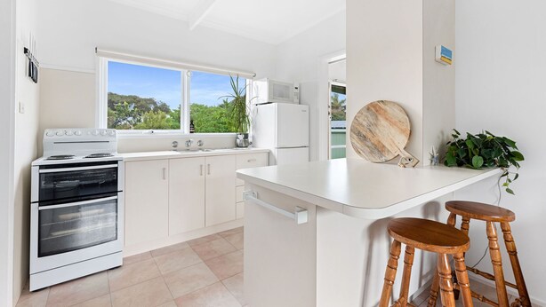 A modern kitchen with a built-in oven, a microwave, and a refrigerator. There is a large window providing a view of greenery outside. - Tyrone Beach Escape (Rye)
