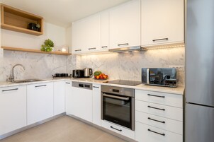 A modern kitchen with white cabinets, a stainless steel refrigerator, a built-in oven, and a coffee maker.