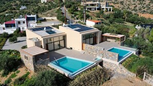 Une maison moderne dotée de deux piscines, de panneaux solaires et offrant une vue sur les collines.