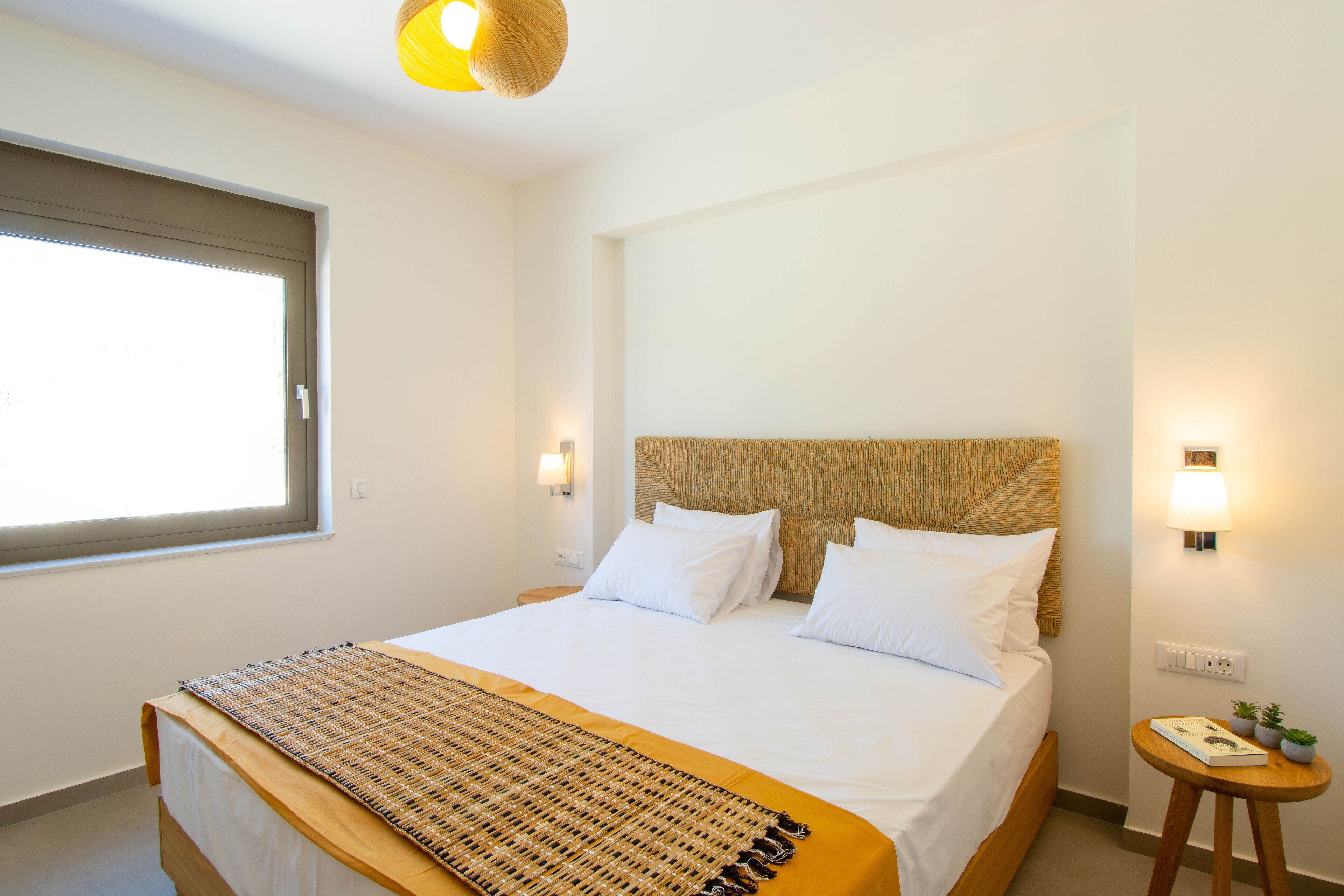 Ein ordentlich eingerichtetes Schlafzimmer mit einem großen Bett, einem Nachttisch mit Lampe und einem Fenster, das für natürliches Licht sorgt.