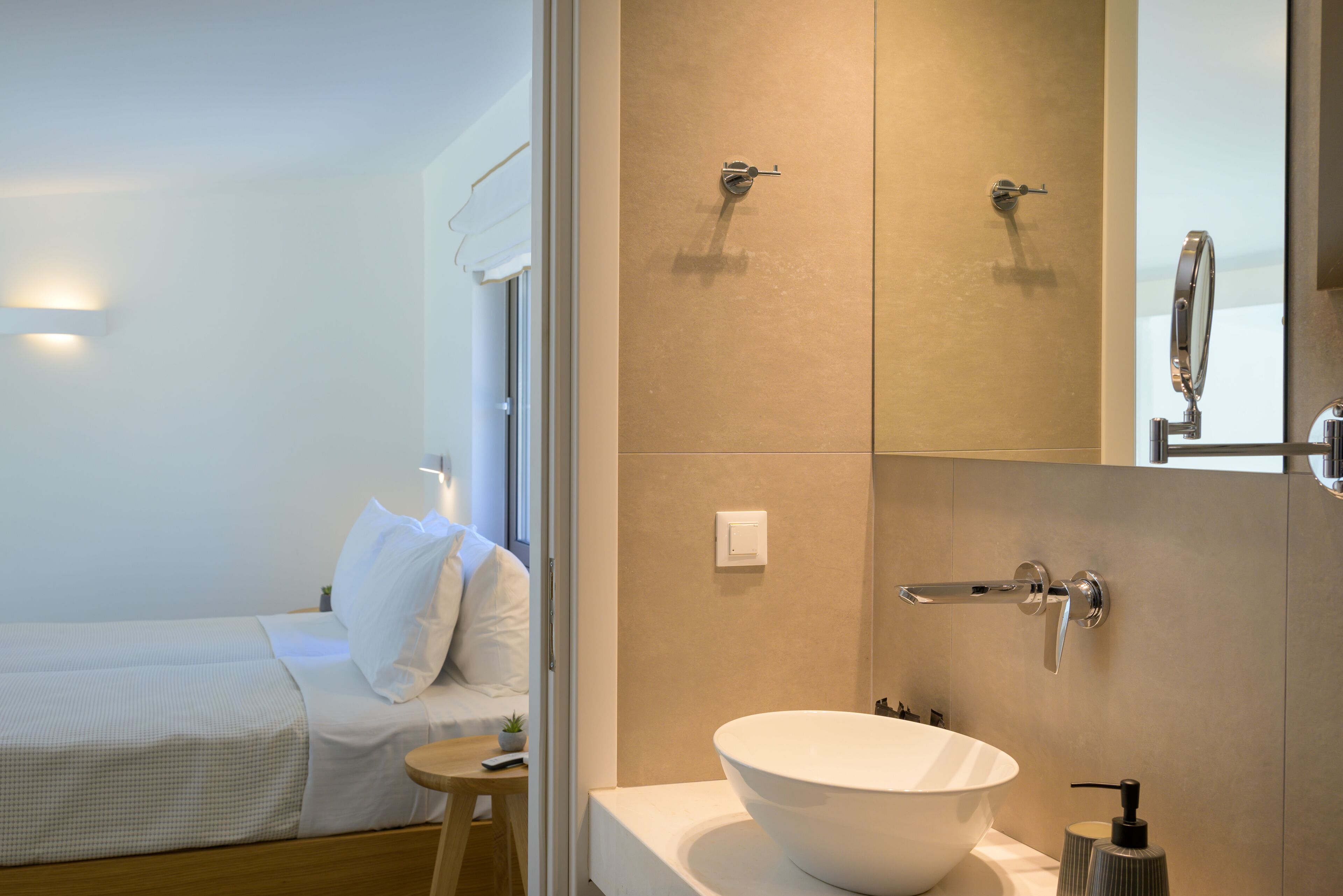 Een moderne hotelkamer met een grote witte wastafel, een bed met witte lakens en een klein nachtkastje.