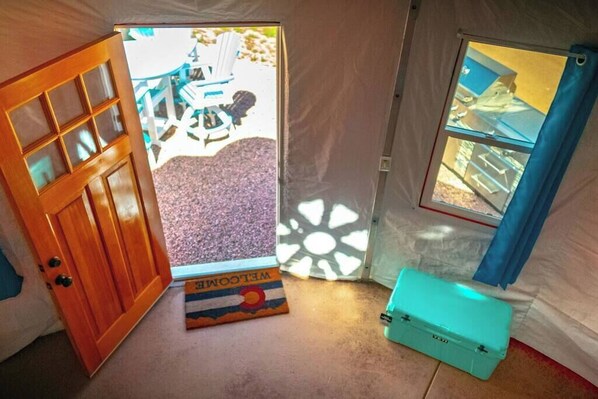 A tent with a wooden door, a welcome mat, and a turquoise toolbox.