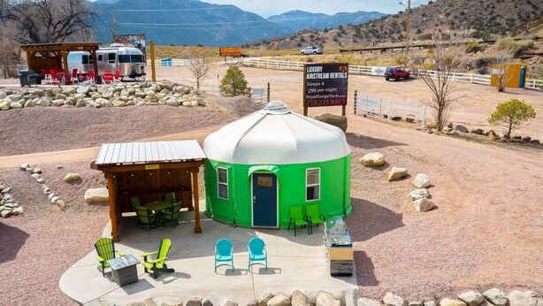 A green and white Airstream RV with a covered outdoor seating area, surrounded by rocks and a mountainous backdrop.
