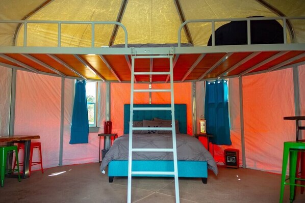 A tent with a bunk bed, a ladder, and a small table with a chair.