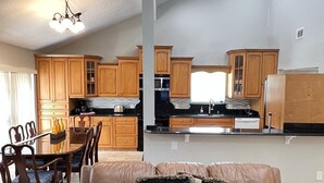 Un soggiorno spazioso con un divano in pelle e una zona pranzo con sedie in legno e un tavolo in vetro. Sullo sfondo, si intravede una cucina con mobili in legno e un piano di lavoro nero.