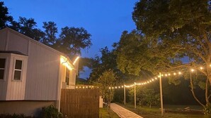 Una casa con un vialetto lastricato che conduce a un patio in legno, circondata da alberi e luci decorative.