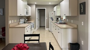 A modern kitchen with white cabinets, a microwave, and a refrigerator. There is a dining area with a table and chairs.