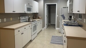 A modern kitchen with white cabinets, a built-in microwave, stove, and oven. There is a sink with a dish rack and a striped rug on the floor.