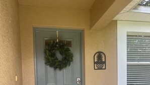 A grey door with a wreath, a welcome sign, and a window with blinds.