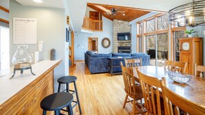 Une cuisine moderne avec une cheminée en pierre, un plafond en bois et un coin repas comprenant une grande table et des tabourets de bar.