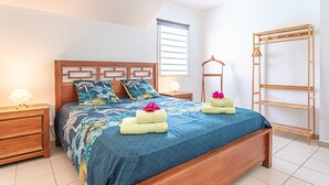 A bedroom with a wooden bed, a nightstand, a wooden wardrobe, and a window with blinds. - Ô Rêves Bleus - Two Bedroom Apartment, Sleeps 4 (Saint-Francois)