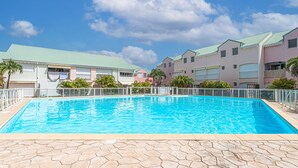 A swimming pool with a tiled deck, surrounded by buildings with green roofs and balconies. - Ô Rêves Bleus - Two Bedroom Apartment, Sleeps 4 (Saint-Francois)