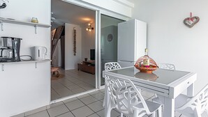 A modern kitchen with white cabinetry, a coffee maker, and a kettle. There is a dining area with a glass table and white chairs. - Ô Rêves Bleus - Two Bedroom Apartment, Sleeps 4 (Saint-Francois)