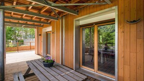 Una terraza de madera con una mesa y sillas, puertas correderas de vidrio amplias y vistas a un jardín.