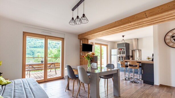 Una cocina moderna con comedor, vigas de madera y un amplio ventanal con vistas a la vegetación.