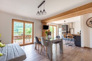 Una cocina moderna con comedor, vigas de madera y un amplio ventanal con vistas a la vegetación.