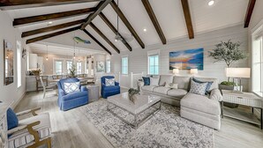 A spacious living room with a high ceiling, wooden beams, a large coffee table, and a view of the kitchen and dining area through an open layout. - Beautiful golf course view home at Palmilla Beach Resort with resort pool (Port Aransas)