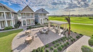 A large house with a patio area, a pool, and a view of a golf course. - Beautiful golf course view home at Palmilla Beach Resort with resort pool (Port Aransas)