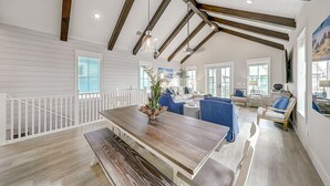 A spacious living area with a wooden dining table, blue sofas, and a white railing. - Beautiful golf course view home at Palmilla Beach Resort with resort pool (Port Aransas)