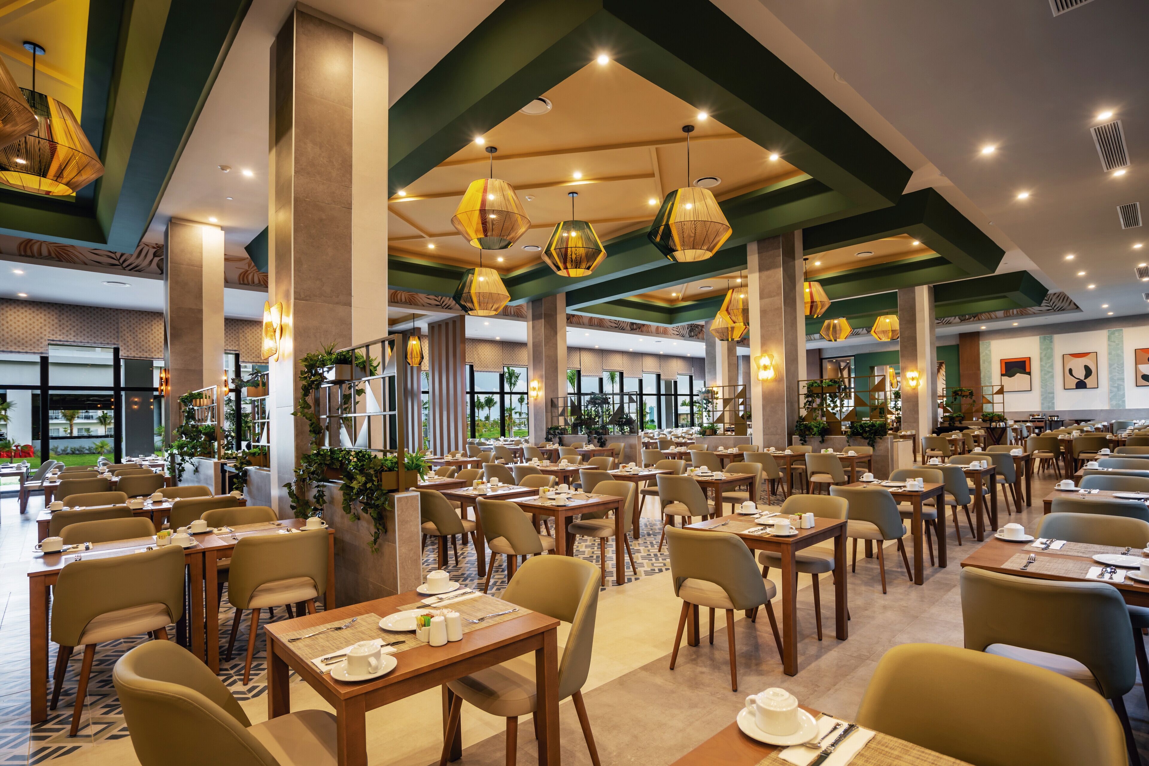 Un restaurante espacioso con varias mesas y sillas, ventanas amplias y lámparas colgantes.