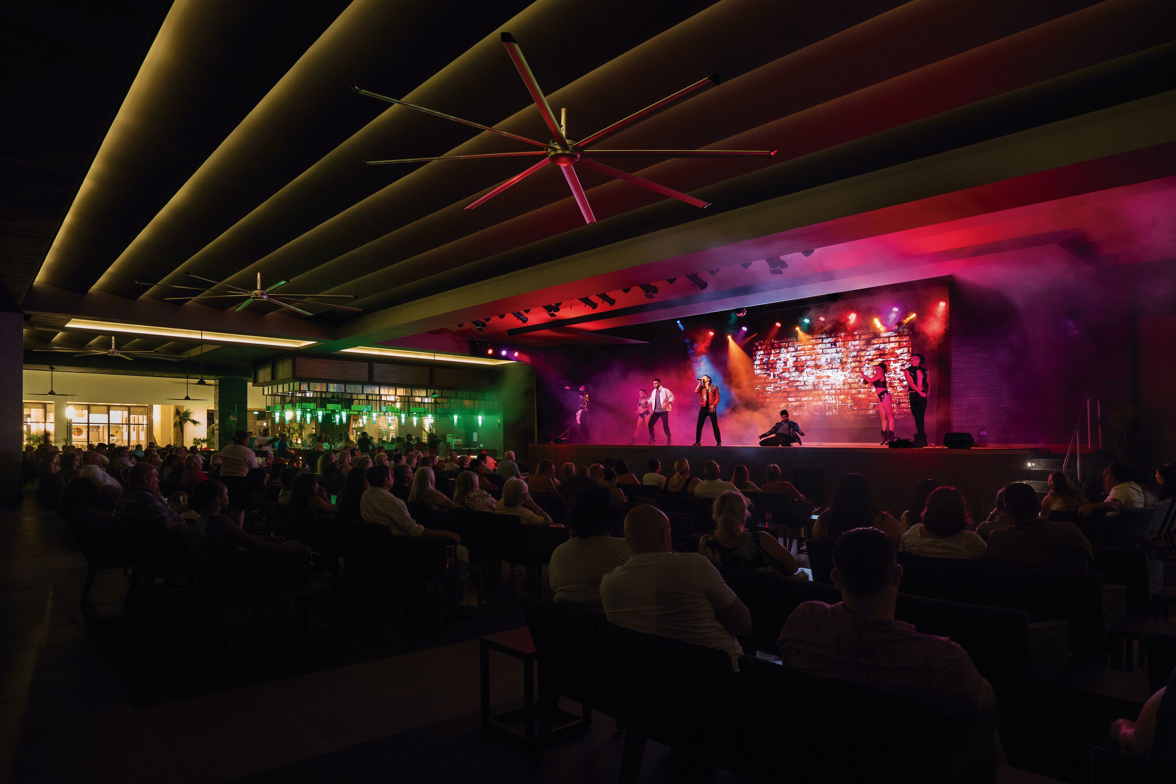 Ein geräumiges Auditorium mit abgestuften Sitzreihen, einer Bühne und Darstellern sowie einem modernen Deckenbau.