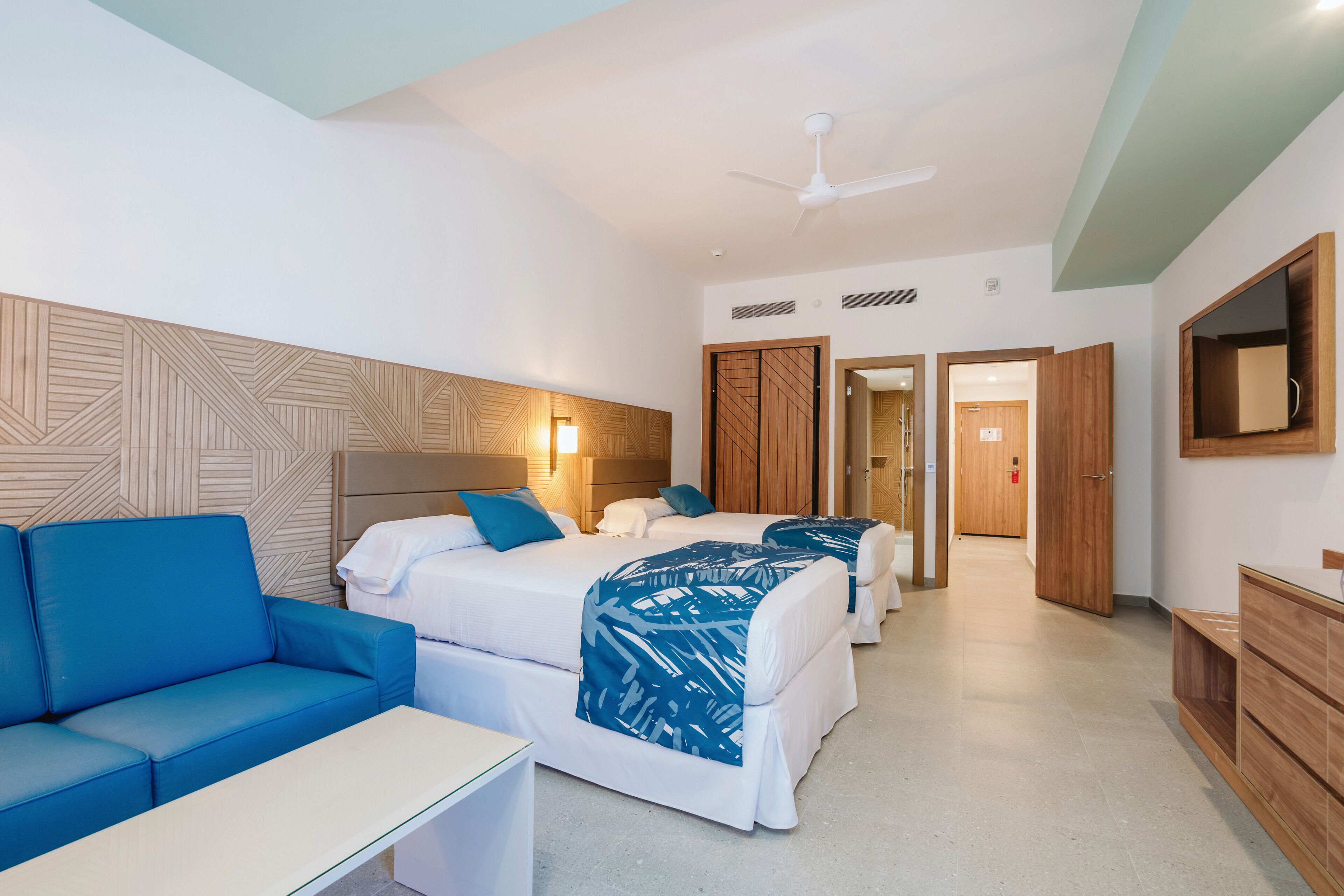 Una habitación de hotel con sofá, dos camas, un escritorio y un armario.