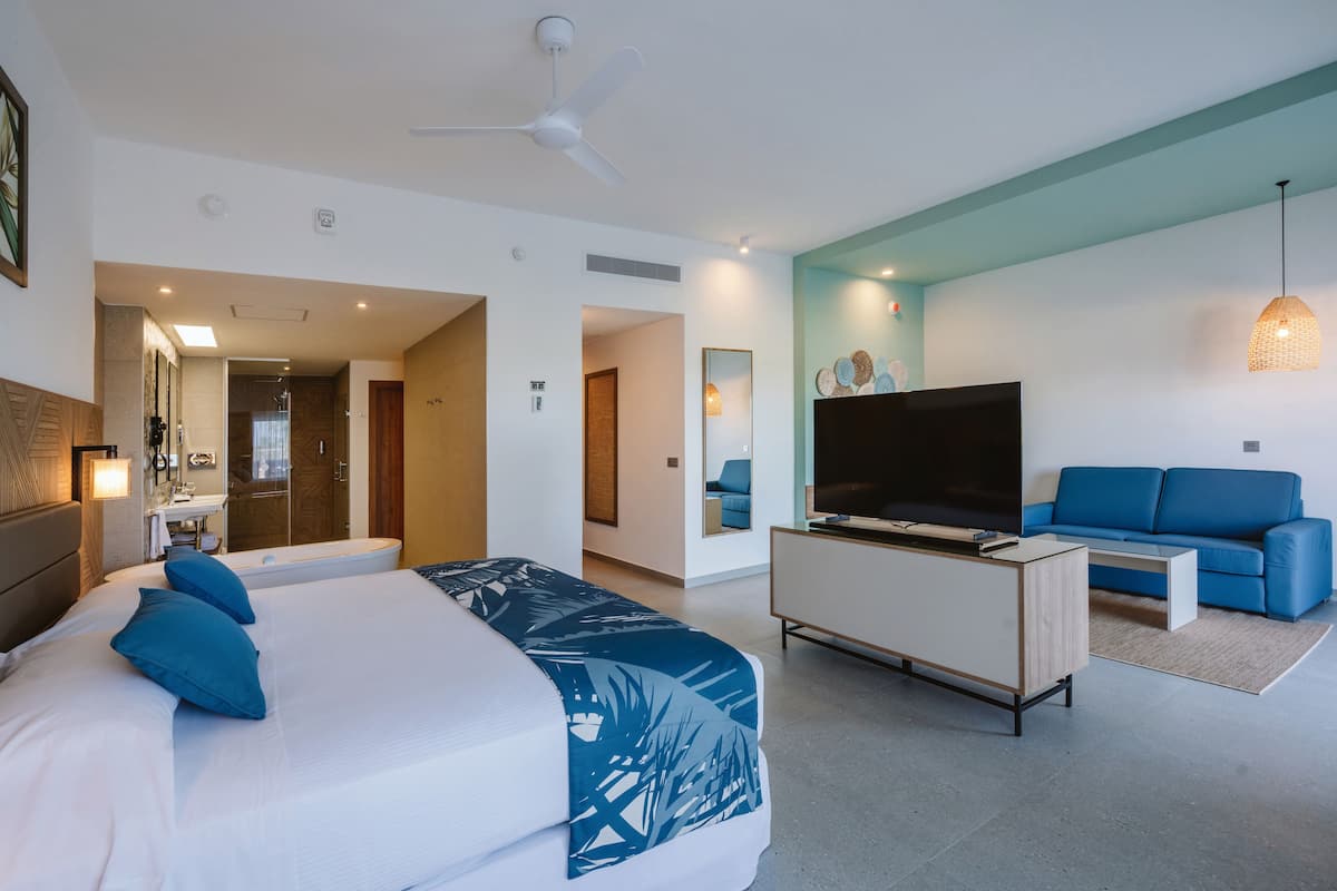 A modern hotel room with a large bed, a TV, a sofa, and a ceiling fan.