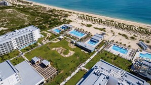 Vista aérea de un complejo turístico con varias piscinas, una playa y un gran edificio de hotel.