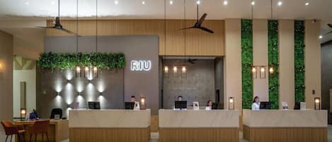 Un área de recepción moderna con un mostrador de madera, un jardín vertical verde y varios ventiladores de techo.