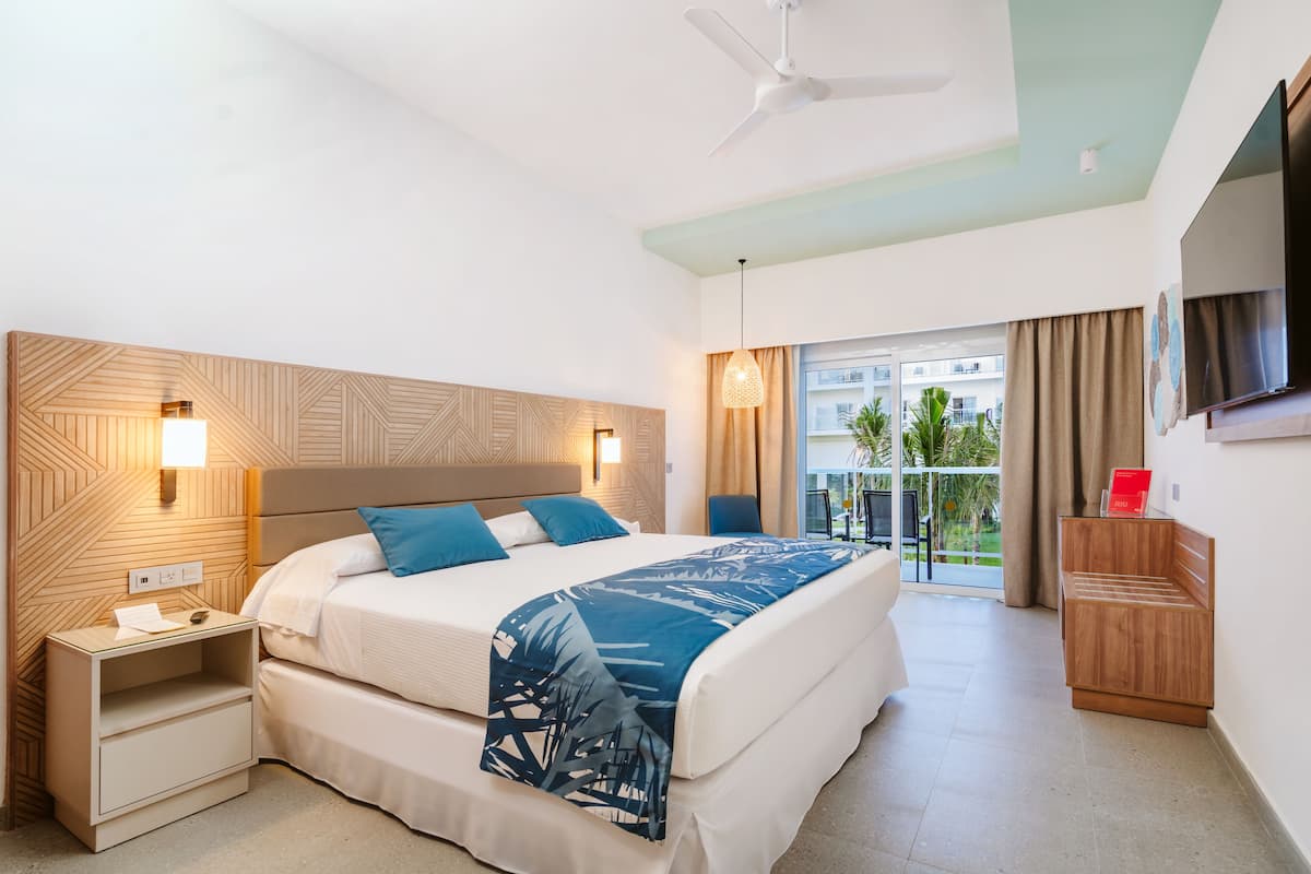 A hotel room with a bed, bedside tables, a TV, and a balcony with a view.