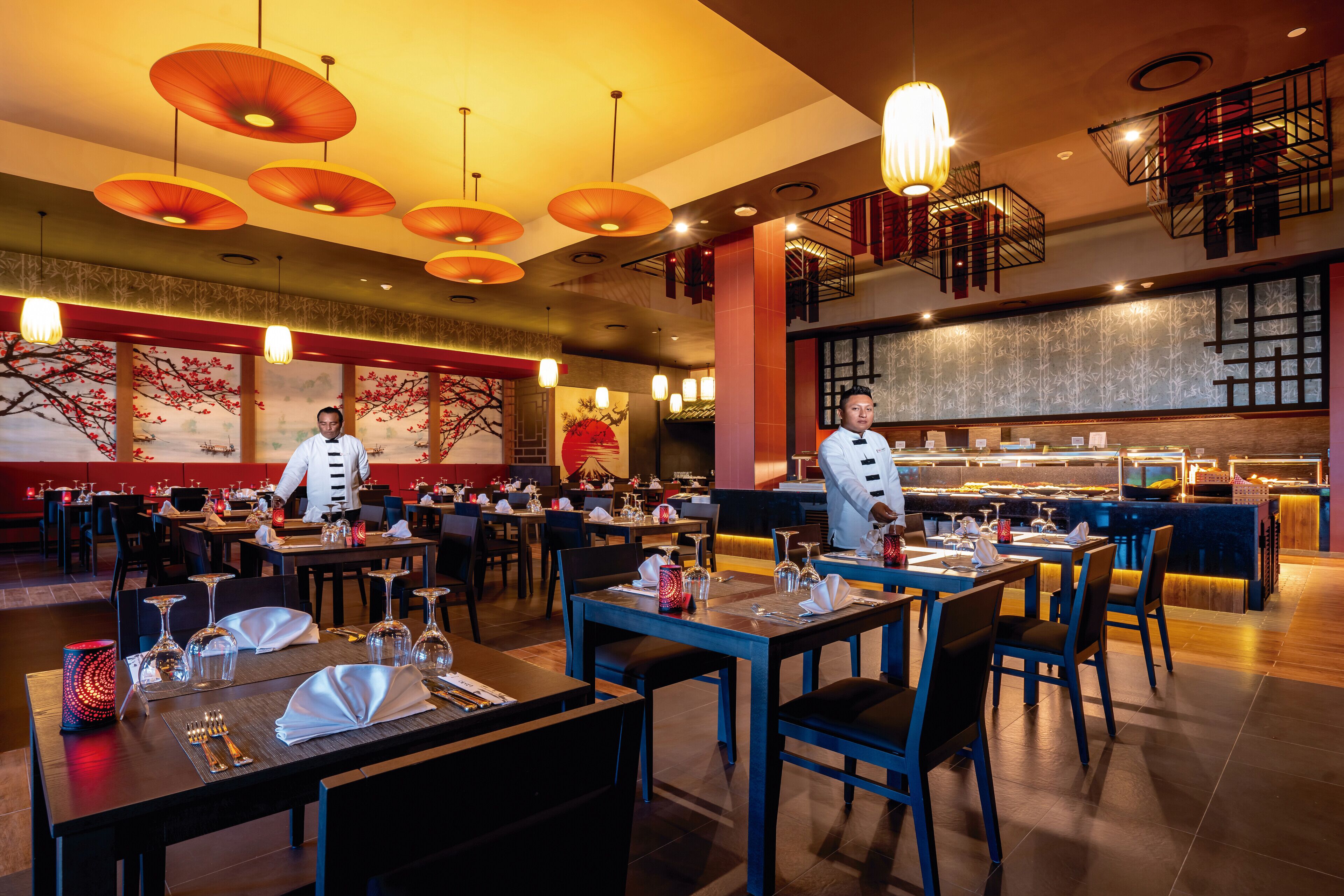 Un restaurante con varias mesas, personal de servicio y una zona de bufé.