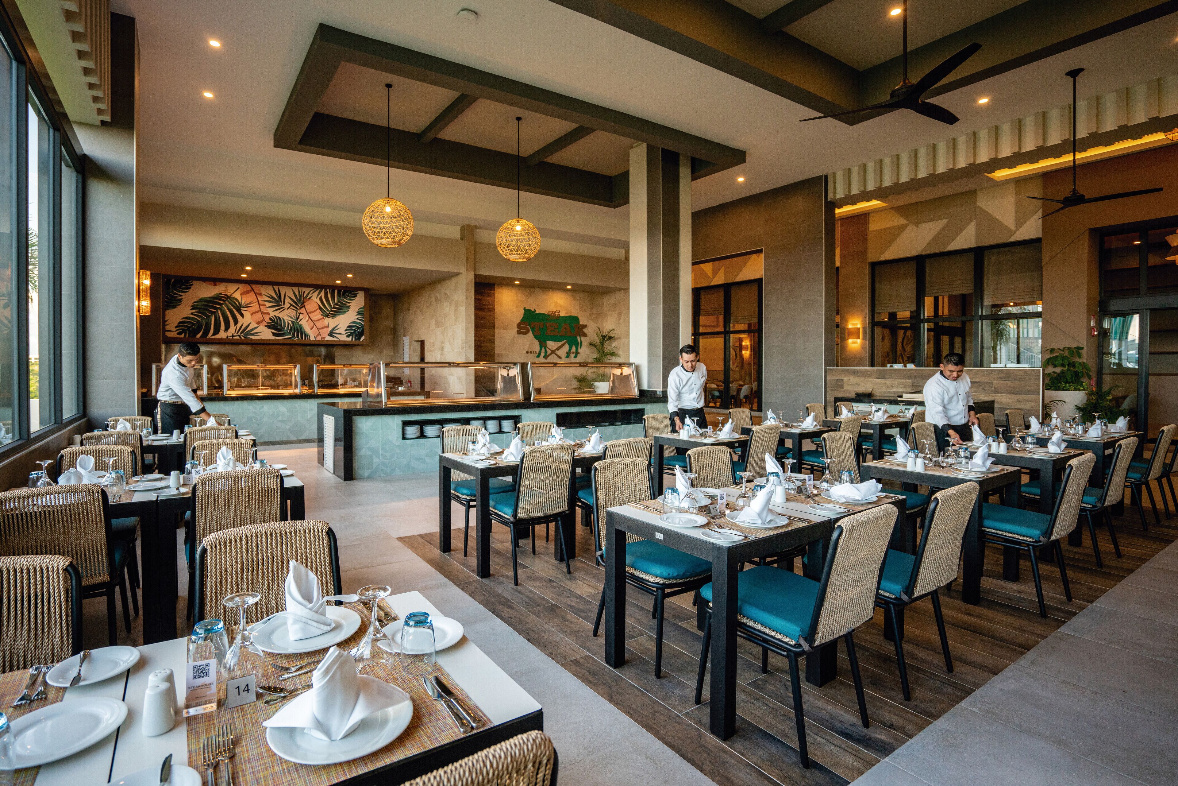 Un restaurante con mesas dispuestas para comer, una zona de bar y una cocina al fondo.