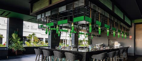 Zona bar moderna con un bancone alto, diversi sgabelli e vista su un’area esterna con piante.