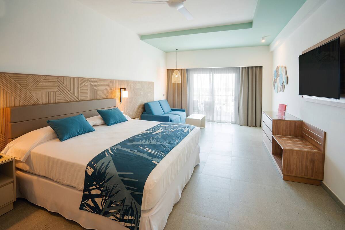 A hotel room with a large bed, a desk, a chair, and a TV.