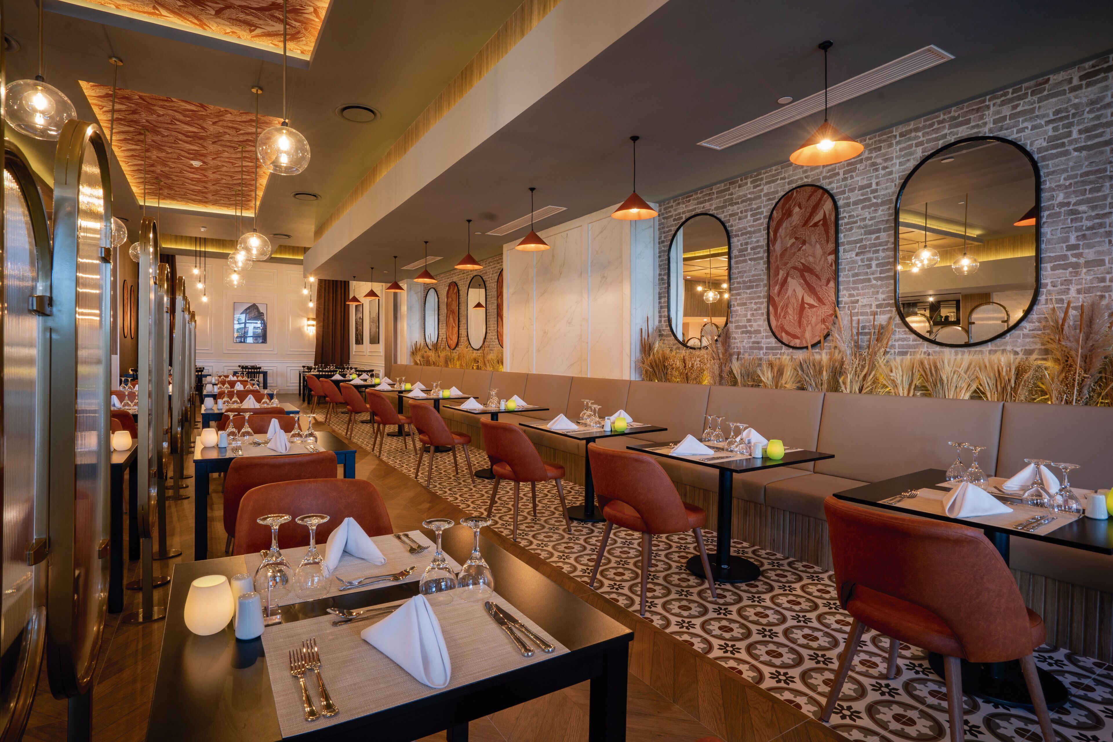 A restaurant with long communal tables, red chairs, and a patterned carpet.