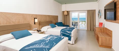 A hotel room with two beds, a TV, a desk, and a balcony with a view of the sea.