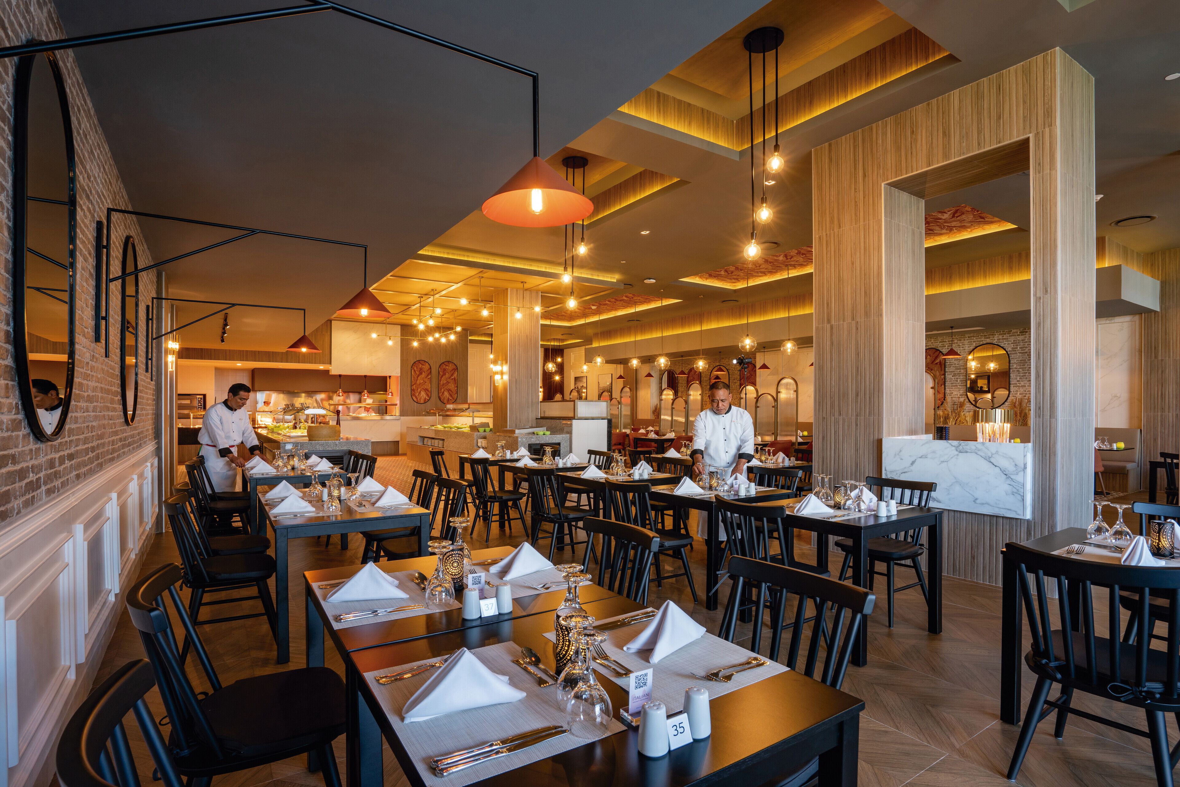 Un restaurante con varias mesas dispuestas, adornadas con servilletas blancas, cubiertos y copas.