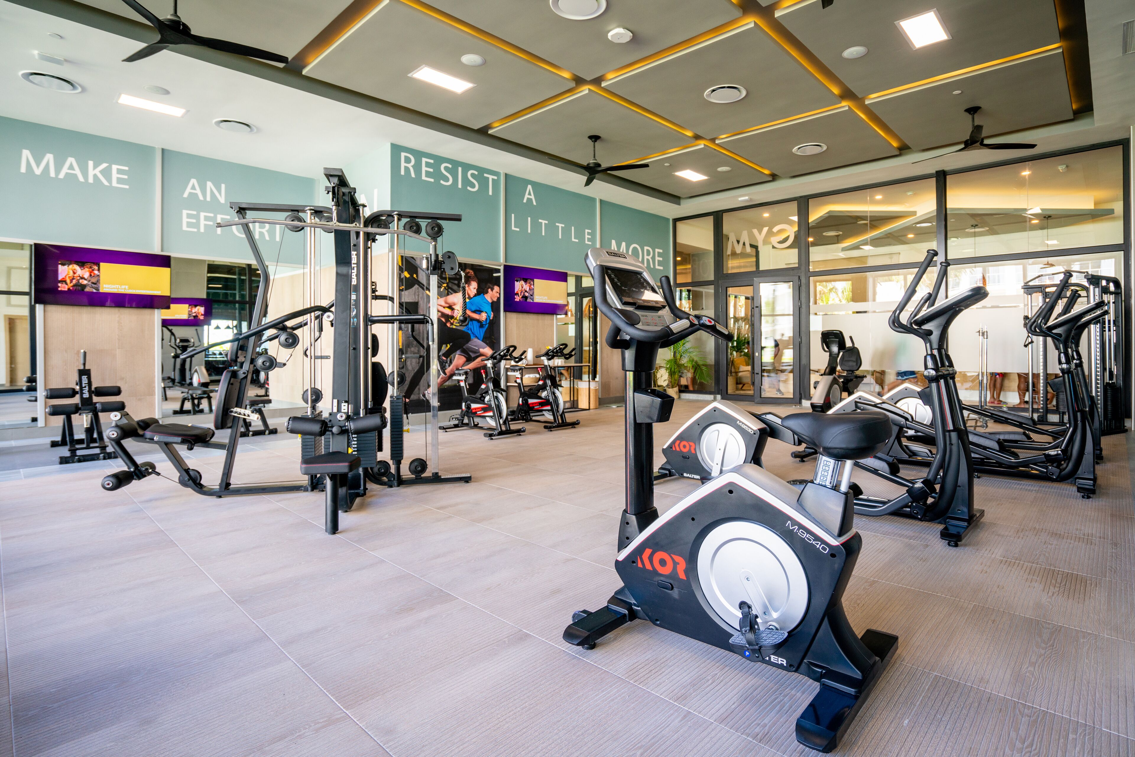 A modern gym with various exercise equipment, motivational wall text, and a clean, spacious layout.