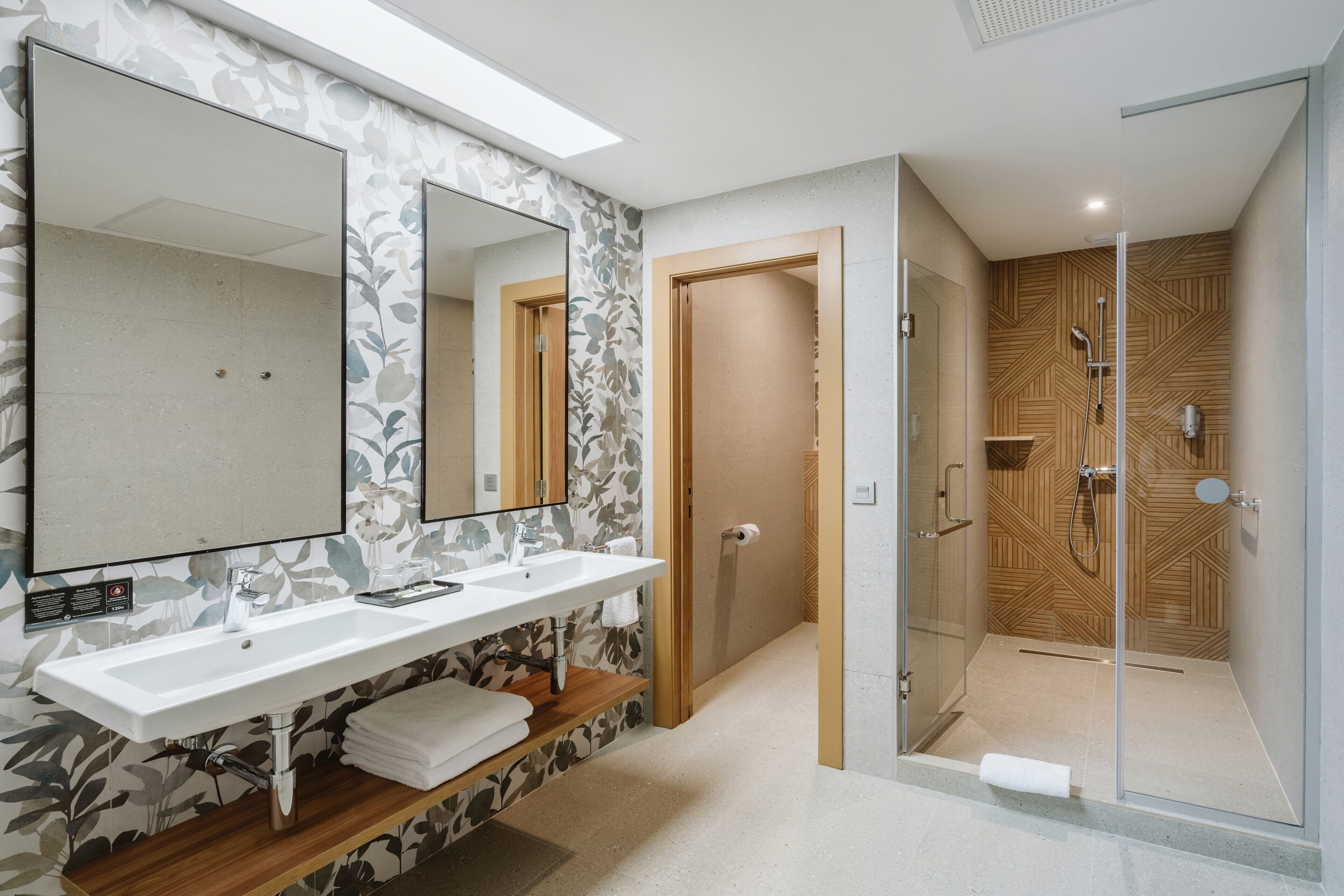 A modern bathroom with a large mirror, two sinks, a shower, and a wooden vanity.