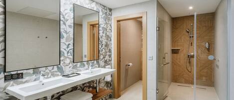 A modern bathroom with a large mirror, two sinks, a shower, and a wooden vanity.