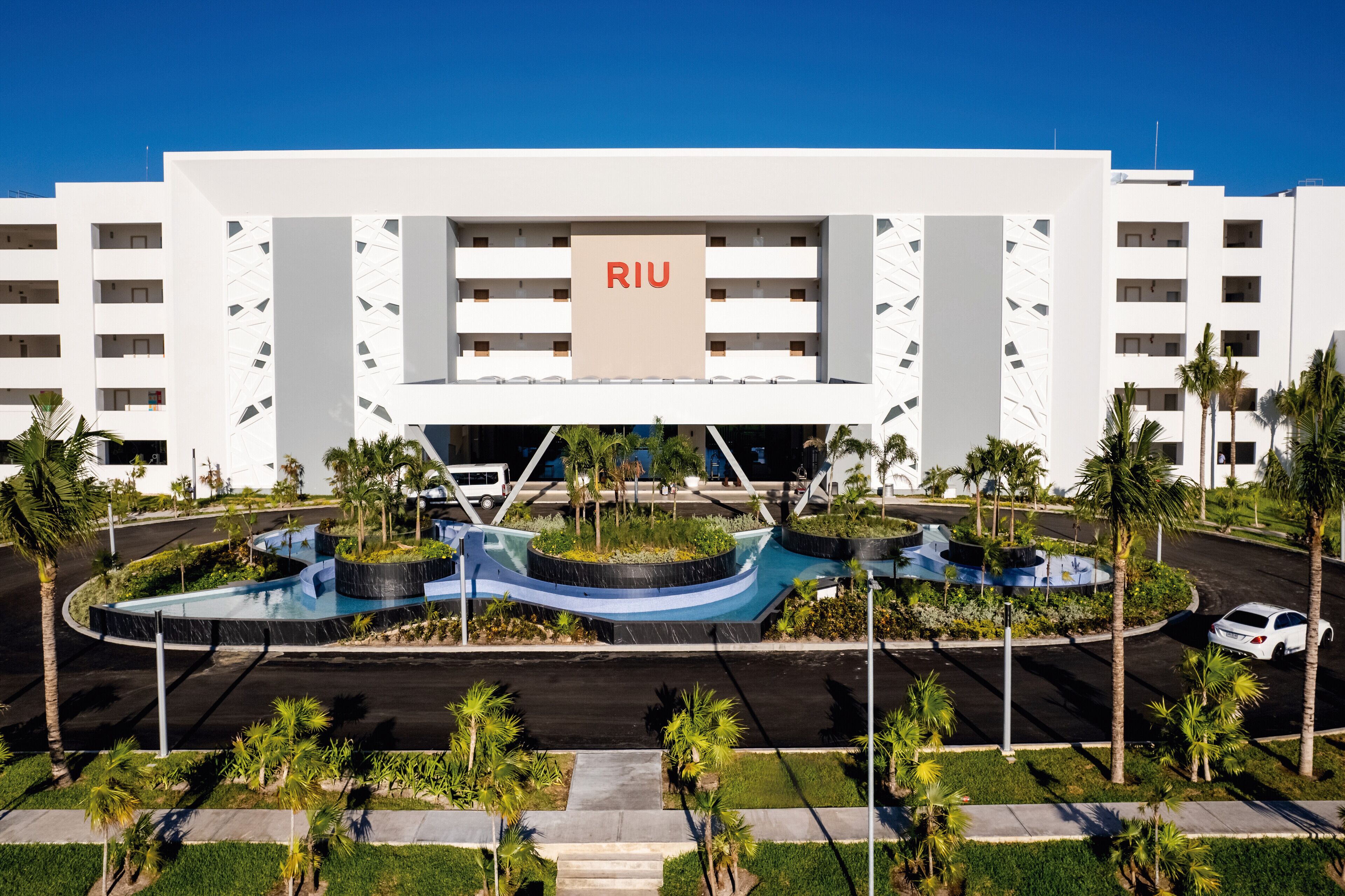 A modern hotel with a central courtyard, palm trees, and a clear blue sky.