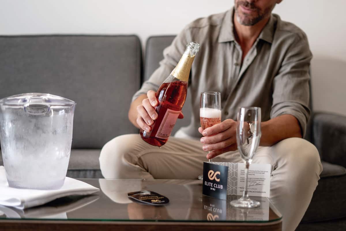 A person pouring a drink into a glass on a glass table with a remote control and a card labeled "ELITE CLUB" in the background.