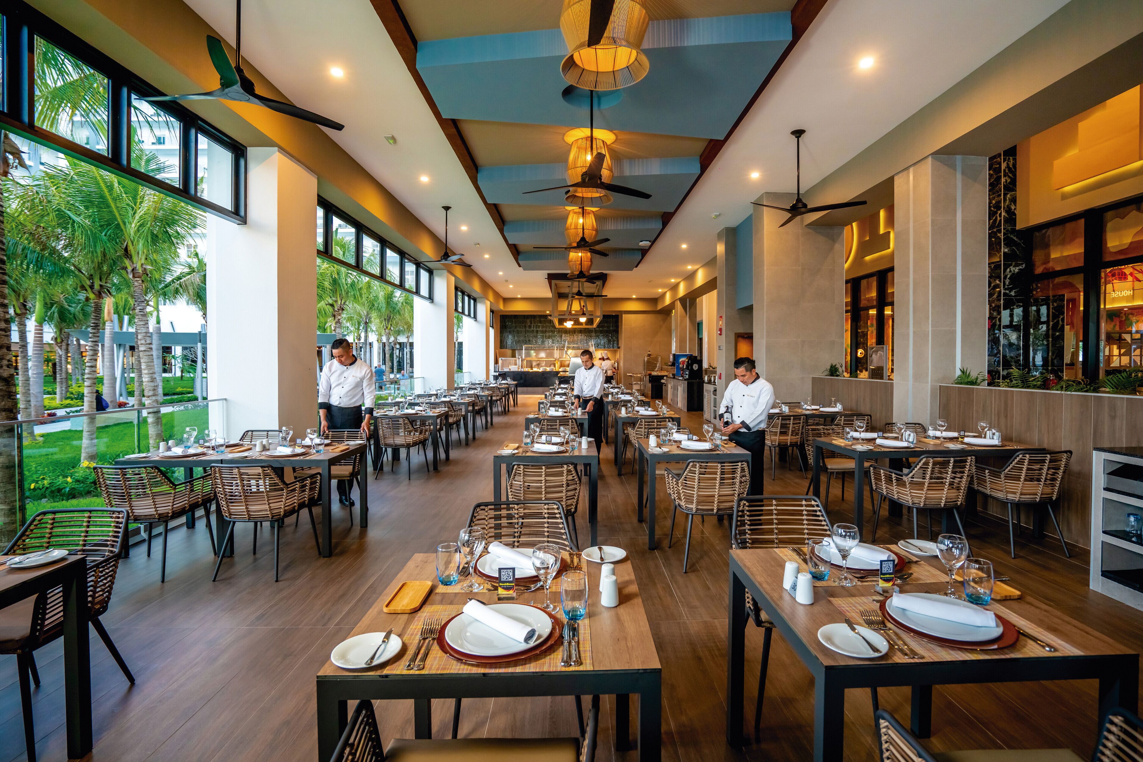 A spacious restaurant with multiple dining tables, chairs, and ceiling fans.