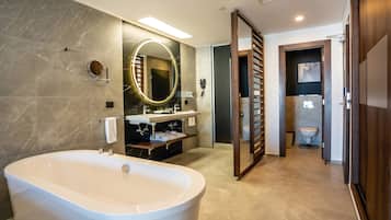 Un baño moderno con una bañera independiente, un tocador con espejo y un inodoro visible a través de una puerta.