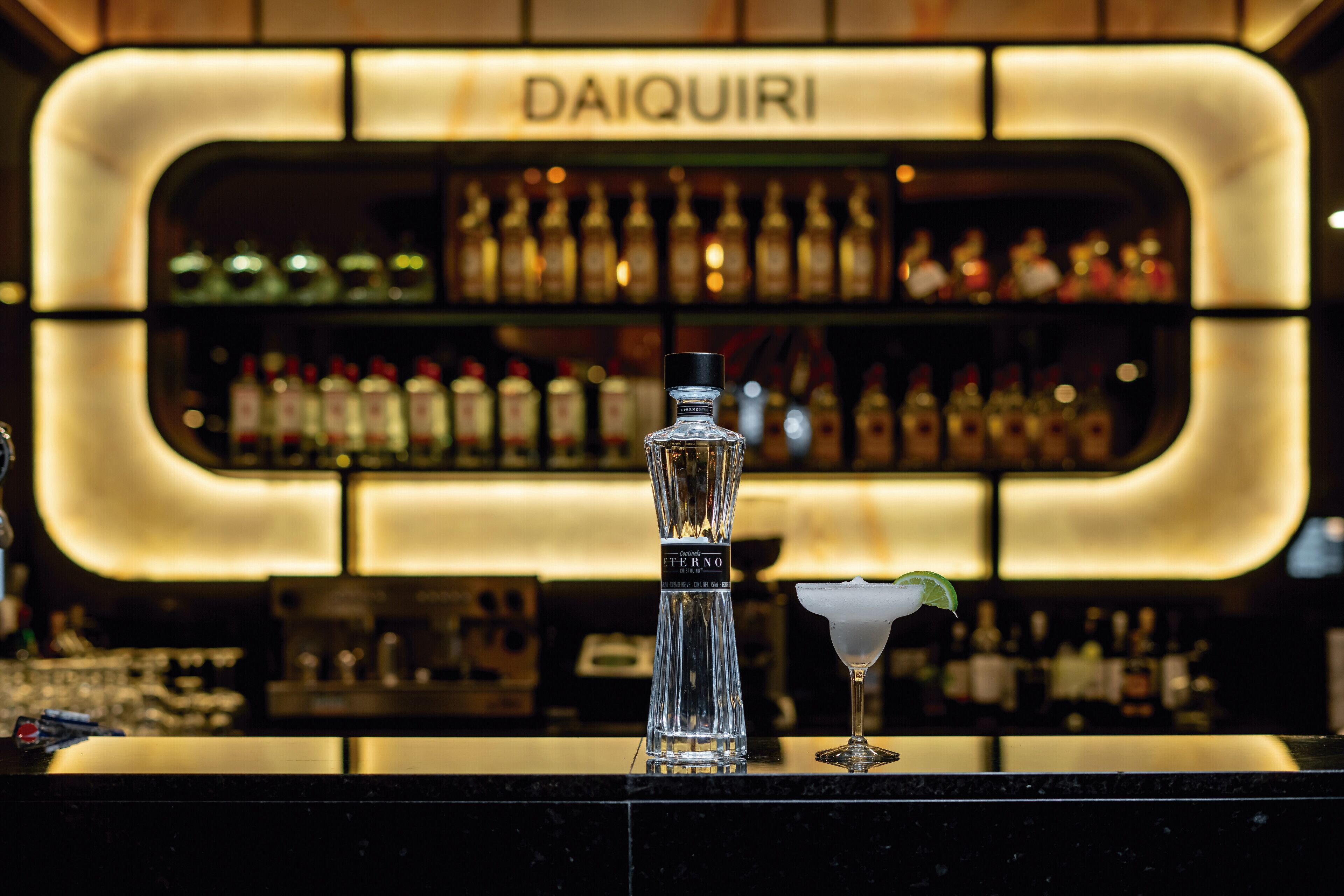 Una zona de bar con una botella de licor y una copa de martini sobre la barra.