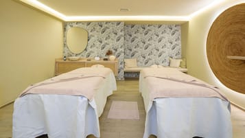 Relax in a serene spa room with two treatment beds, a vanity, and a tropical leaf-patterned accent wall.