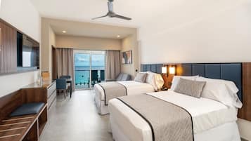 Habitación de hotel con dos camas, un escritorio, una silla, un televisor y un balcón con vista al mar.