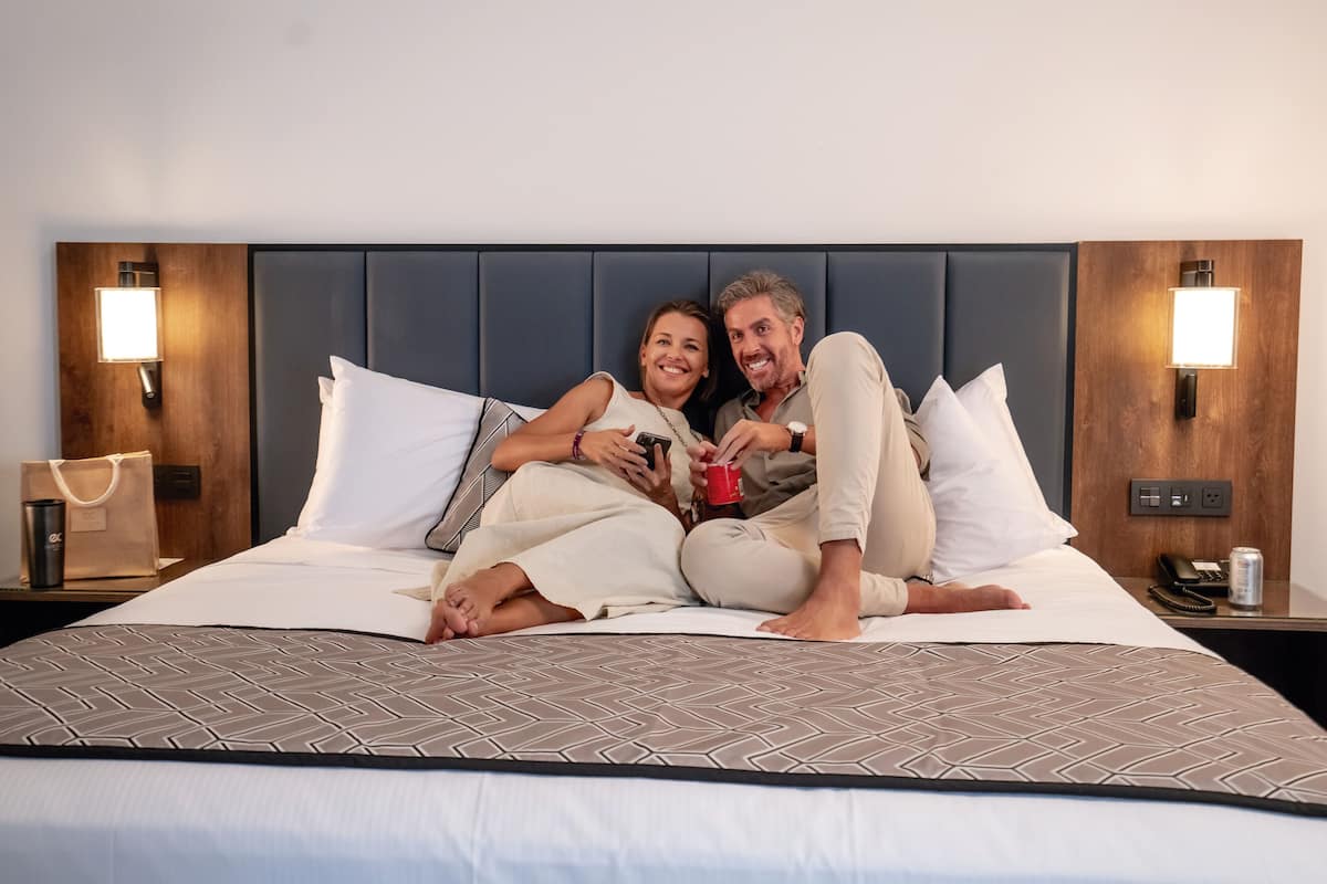 A bed with a patterned bedspread, two bedside tables with lamps, and a wooden headboard.