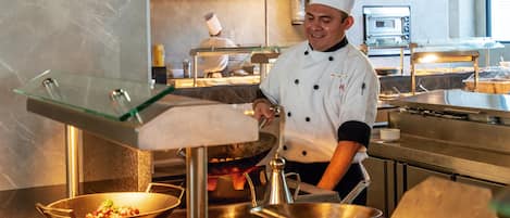 Un chef en una cocina profesional con electrodomésticos de acero inoxidable y una vitrina de vidrio.