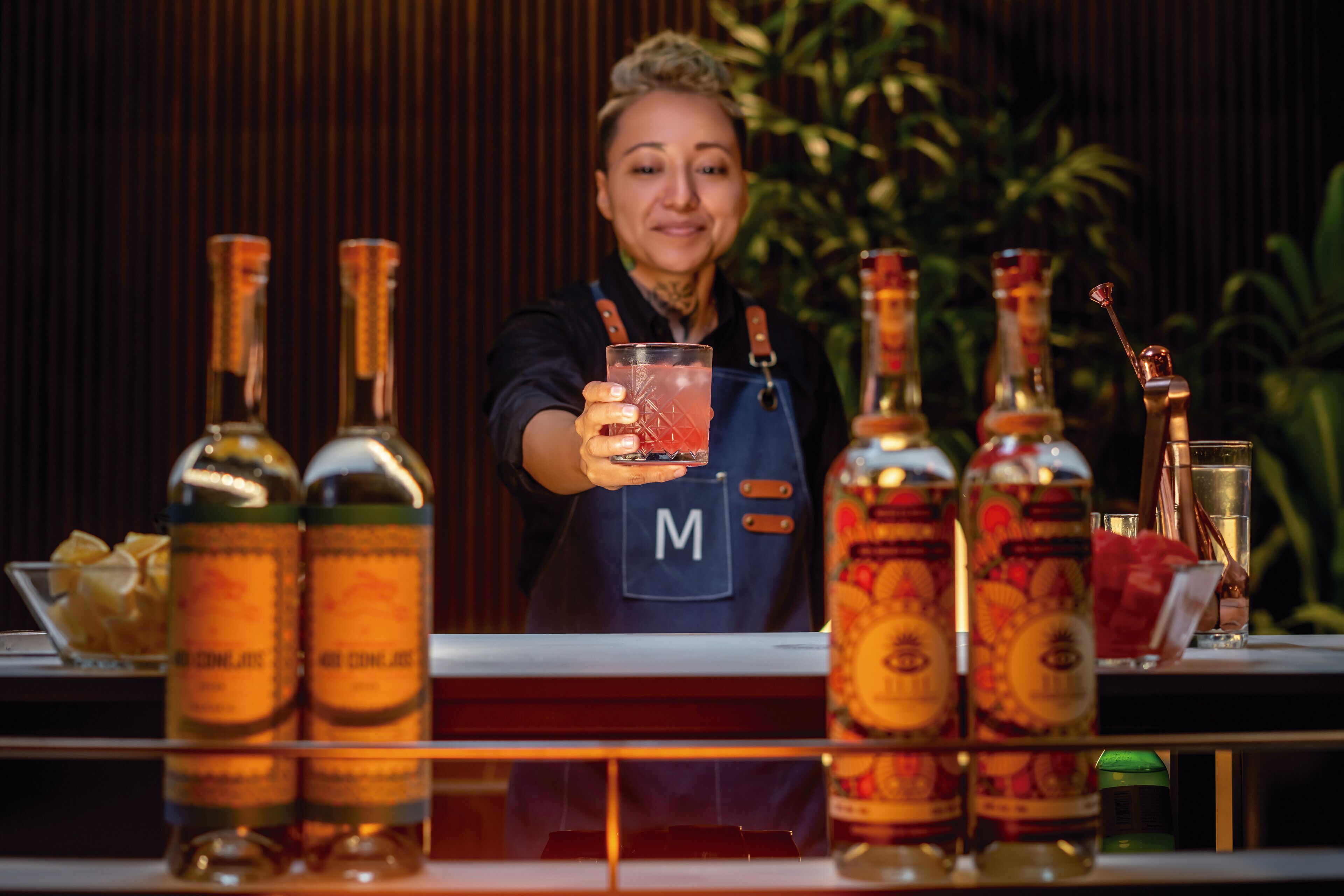 A bartender holding a drink behind a bar with various bottles and glasses.